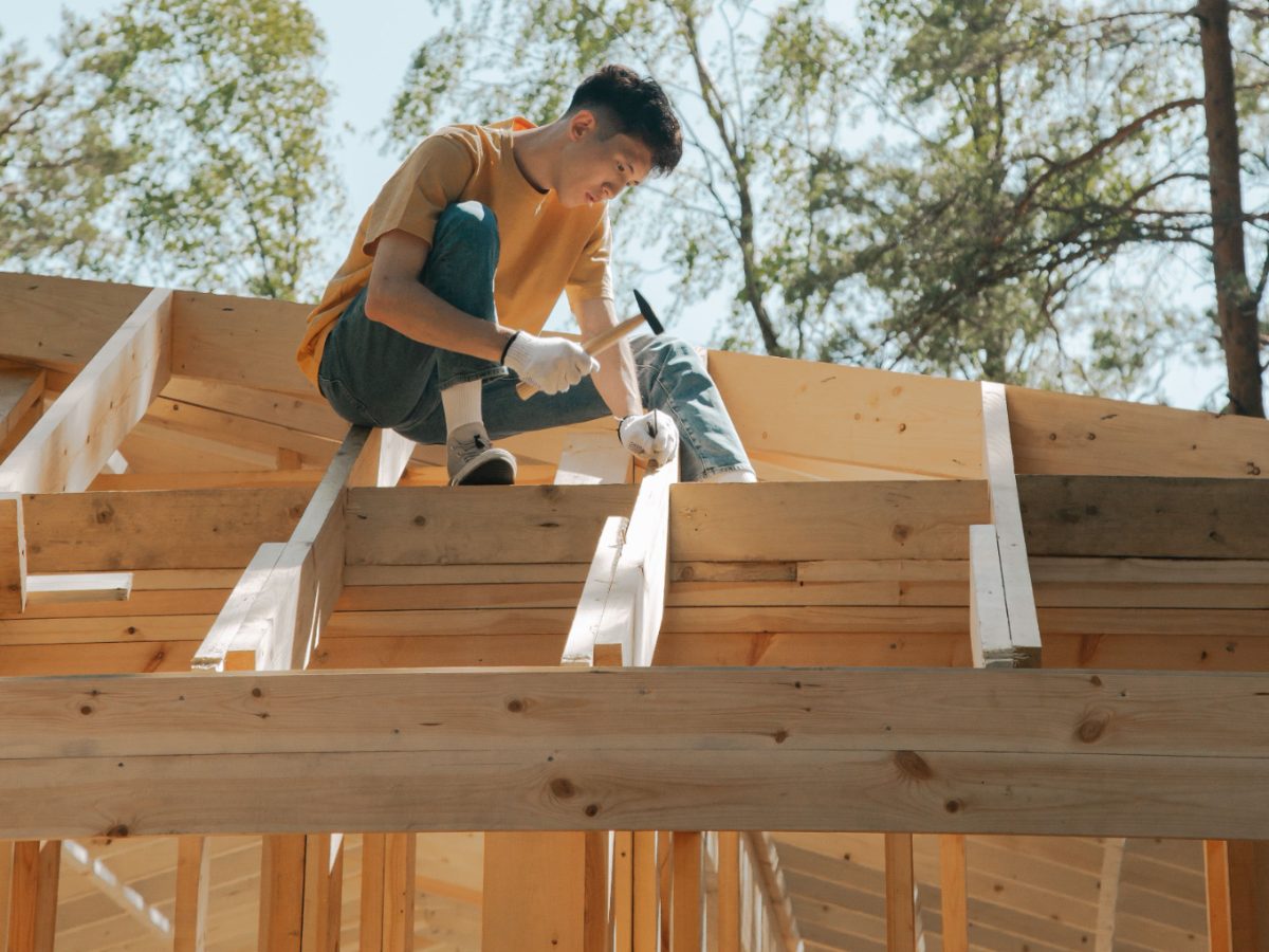 Charpentier au marteau sur la charpente d'une maison en construction : la solidité du gros œuvre, couverte dix ans par la garantie décennale