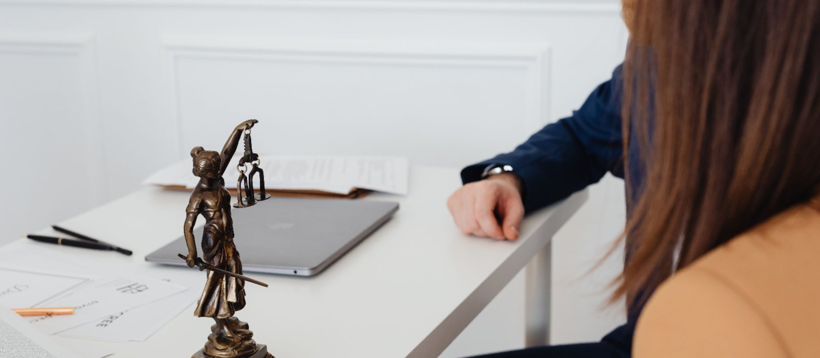 Entretien entre une cliente et son conseil autour d'une table de bureau, statuette de la justice au premier plan